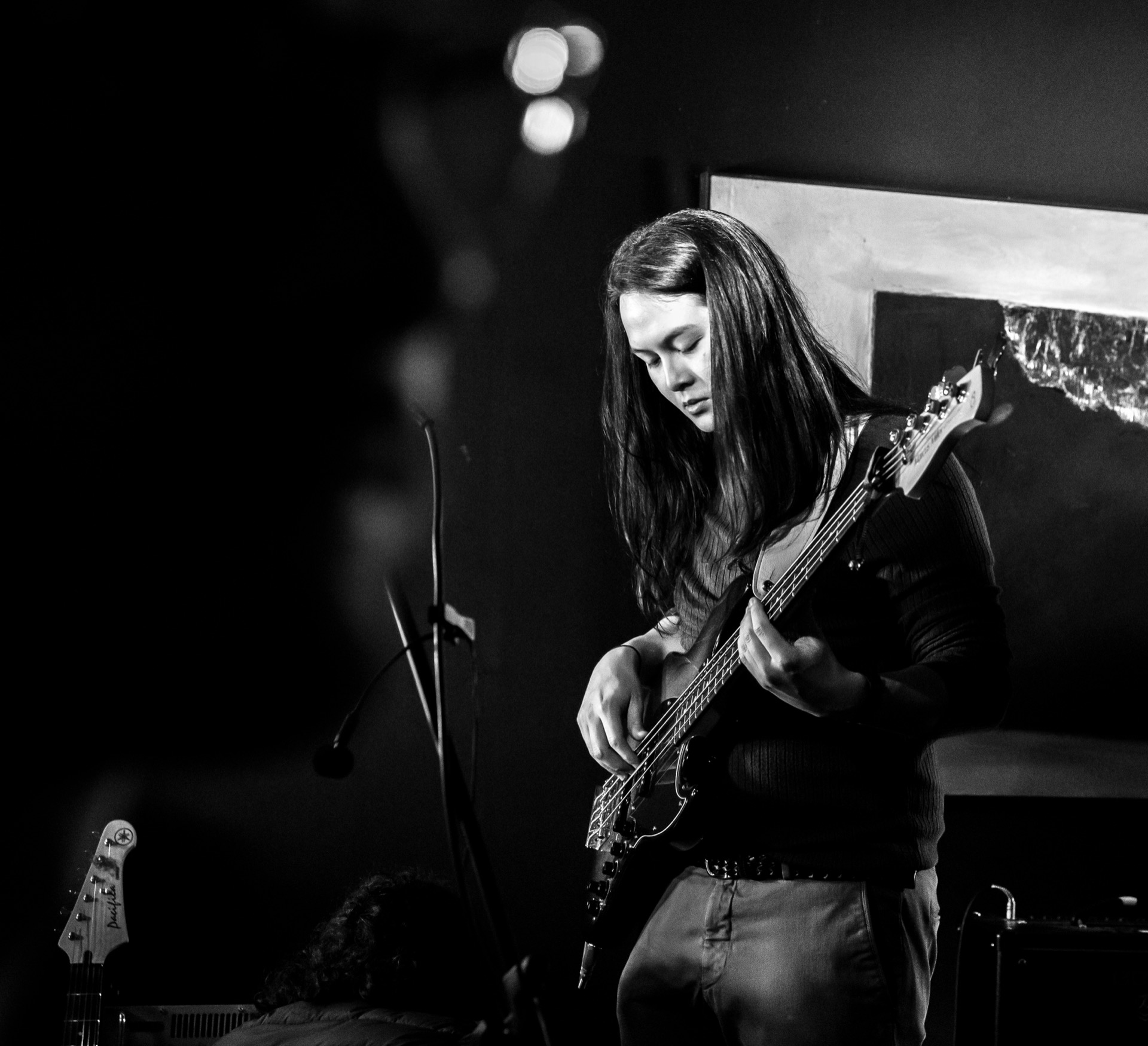 Young woman playing bass guitar at a venue, black and white